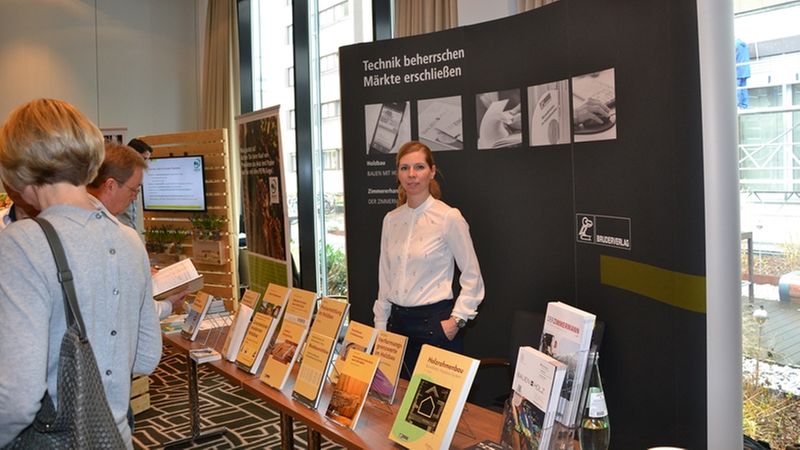 Ein Messestand auf einer Buchmesse mit einer Frau, die hinter einem Tisch mit verschiedenen Büchern steht.