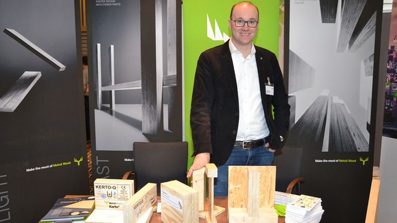 Ein Mann steht an einem Messestand mit Holzmuster und Informationsmaterial.