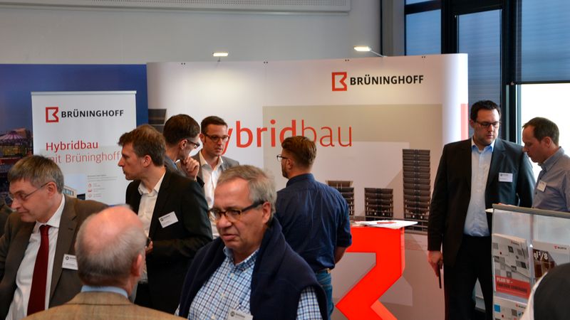 Teilnehmer eines Netzwerktreffens diskutieren vor einem Stand von Brüninghoff über Hybridbau.