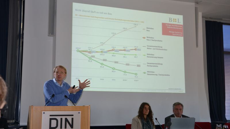 Ein Mann hält eine Präsentation über die Bauwirtschaft, während er vor einem Diagramm spricht, das die Entwicklung in verschiedenen Bau-Segmenten zeigt.