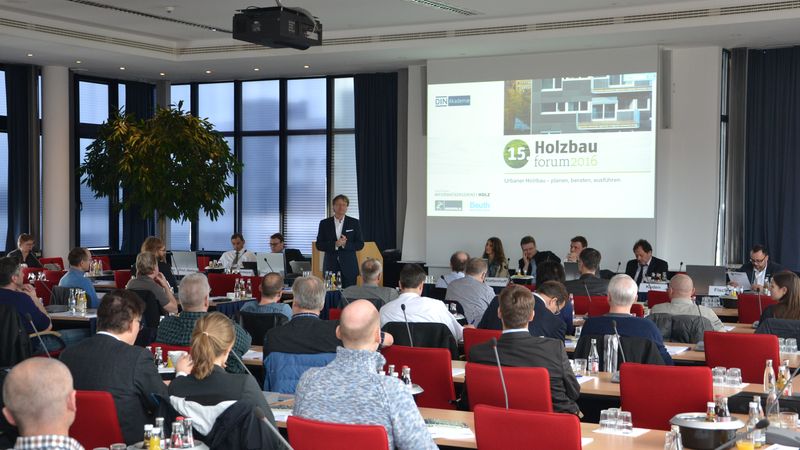 Eine Konferenz mit mehreren Teilnehmern, die einem Vortrag über Holzbau im Konferenzraum folgen.