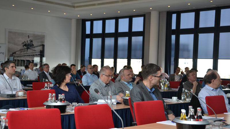 Teilnehmer einer Konferenz in einem modernen Konferenzraum mit roten Stühlen und großen Fenstern.