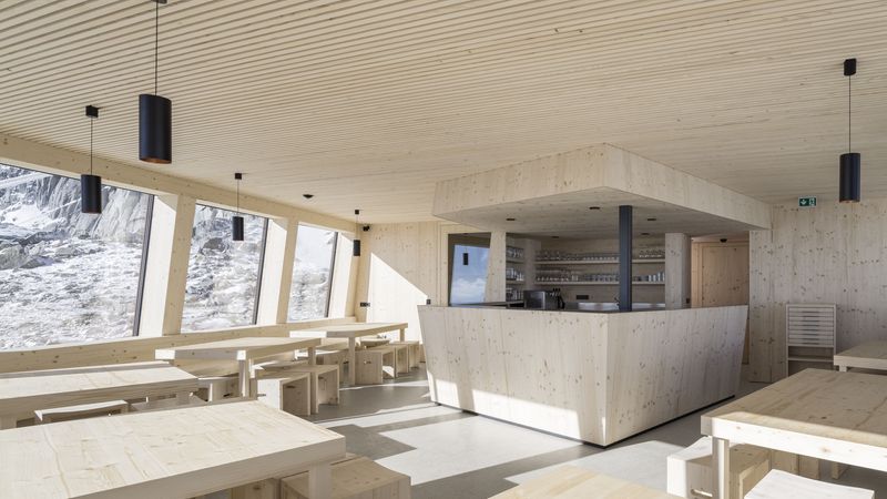 Im lichtdurchfluteten Essbereich gewährt ein durchgehendes Fensterband den Gästen einen 180-Grad-Panoramablick auf die Bergwelt. Im Barbereich erkennt man das Fenster, durch das die Gäste auf der Terrasse bedient werden können. Foto: Velux / Stifter + Bachmann / Oliver Jaist