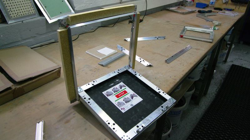 Einsetzen der Klappe: Die Klappe wird an zwei definierten Punkten eingesetzt und mit zwei Sicherungsstanzungen und Fallsicherungen gegen unbeabsichtigtes Aushängen gesichert.