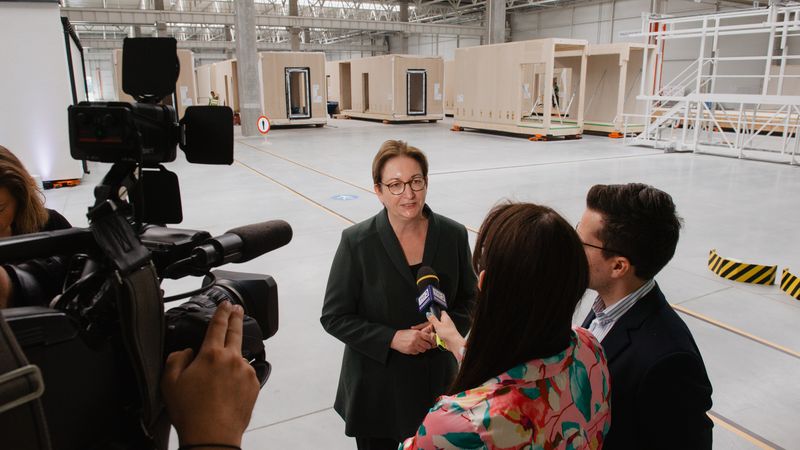 Die Bundesbauministerin setzt auf Modulbau zur schnellen Erstellung von Wohnraum. Im Hintergrund die Module in verschiedenen Größen und Fertigungsstufen.