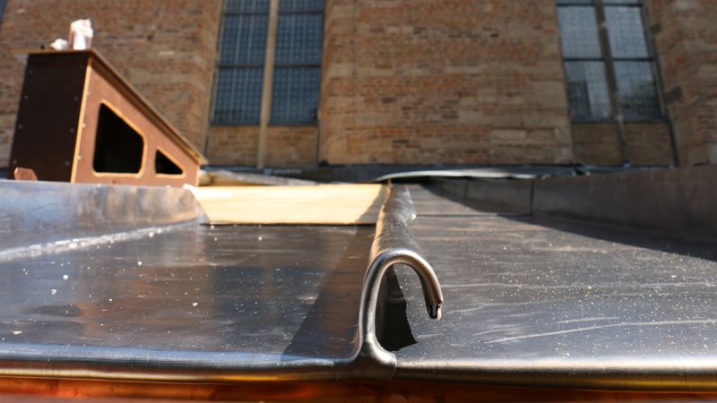 Detailansicht eines Kirchendachs mit Metallverkleidung und Ziegelmauerwerk im Hintergrund.