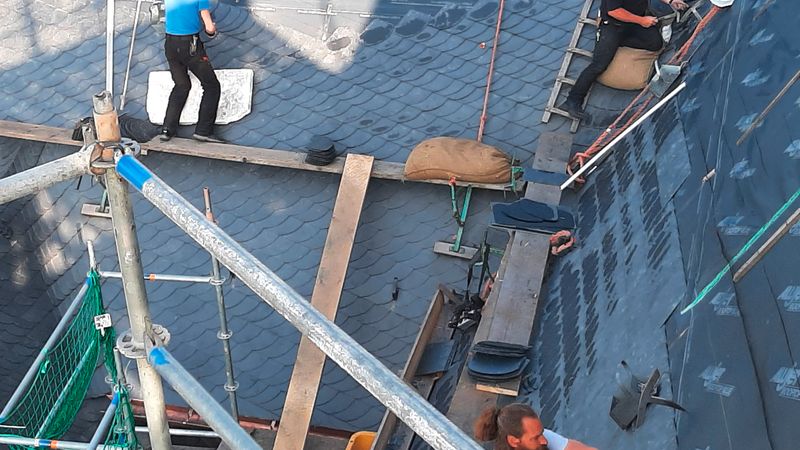 Dachdecker arbeiten auf einem Dach mit Schieferplatten und Gerüst.