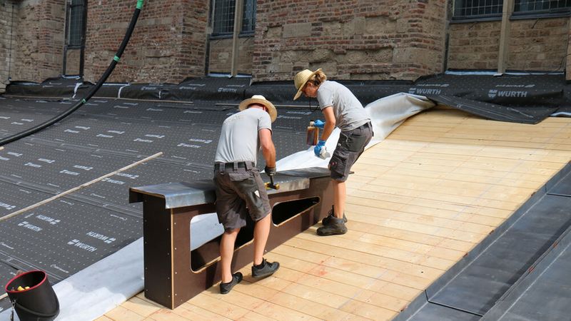 Zwei Handwerker arbeiten auf einem Dach und verlegen eine Schutzfolie.