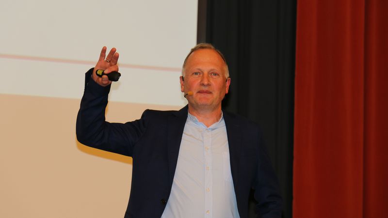 Ein Mann hält einen Vortrag auf einer Bühne und trägt ein Mikrofon.