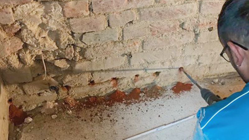 Eine feuchte Wand trocknen: Ein Handwerker setzt Bohrungen für die Horizontalsperre.