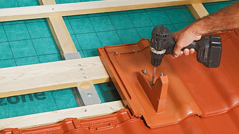 Ein Handwerker befestigt eine Dachplatte mit einem Akkuschrauber auf einer Holzunterkonstruktion.