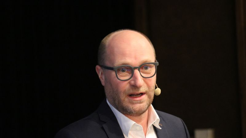 Ein Mann mit Brille und Mikrofon spricht auf einer Bühne.