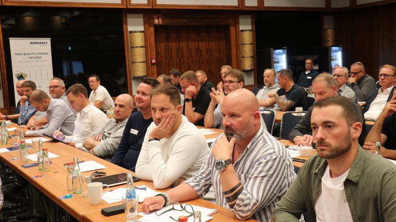 Eine Gruppe von Seminarteilnehmern sitzt aufmerksam in einem Konferenzraum und hört einem Vortrag zu.