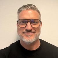 Ein Porträt eines Mannes mit Brille und grauem Haar vor einem neutralen Hintergrund.