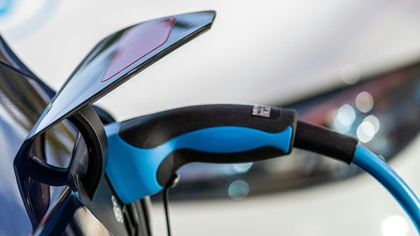 Ein Elektroauto wird an einer Ladestation aufgeladen. Der blaue Ladestecker ist in das Fahrzeug eingesteckt.
