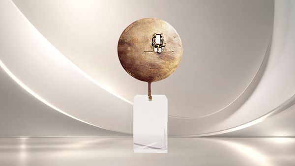 Eine abstrakte, runde Bronzeskulptur mit einer kleinen Durchbruch-Öffnung, die auf einem transparenten Acrylsockel vor einem minimalistischen, hellen Hintergrund präsentiert wird.
