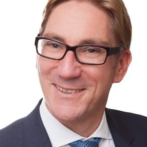 Ein Porträt eines lächelnden Dr. Tobias Rodemann mit Brille, in einem hellen Hemd und dunklen Anzug.