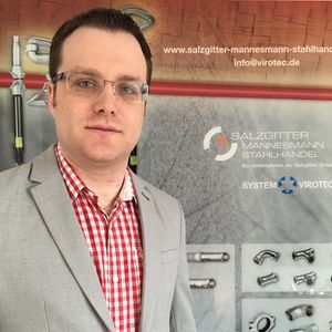 Ein Mann in einem grauen Anzug steht vor einem Werbebanner von Salzgitter Mannesmann Stahlhandel.