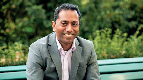 Portrait eines mittelalten Mannes, der auf einer Gartenbank sitzt.