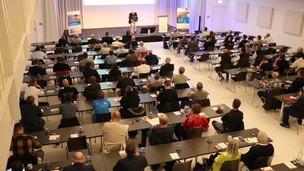 Ein Konferenzraum voller Teilnehmer, die einer Präsentation folgen.