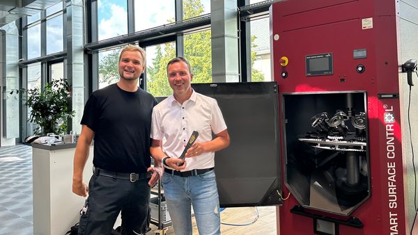 Zwei Männer stehen vor einer großen Maschine in einem modernen, lichtdurchfluteten Raum.