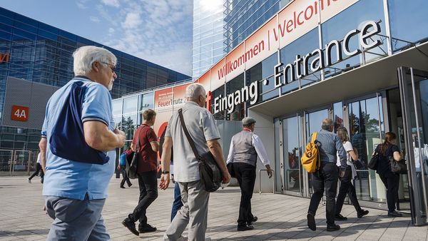 Besucher betreten den Eingang einer Messehalle bei sonnigem Wetter.