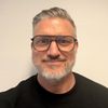 Ein Porträt eines Mannes mit Brille und grauem Haar vor einem neutralen Hintergrund.