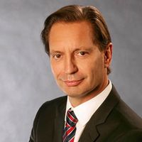 Ein Mann in einem Anzug posiert vor einem neutralen Hintergrund.