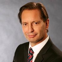 Ein Mann in einem Anzug posiert vor einem neutralen Hintergrund.