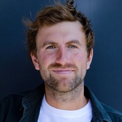 Ein Porträt eines lächelnden Mannes vor einem dunklen Hintergrund.