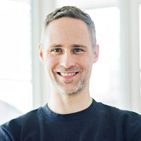 Ein lächelnder Mann steht mit verschränkten Armen in einem modernen Büro.