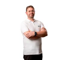 Ein Mann in einem weißen Poloshirt steht mit verschränkten Armen vor einem weißen Hintergrund.