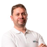 Ein Mann in einem weißen Poloshirt steht mit verschränkten Armen vor einem weißen Hintergrund.