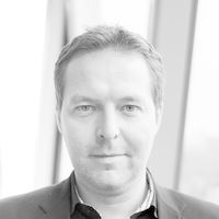 Ein Schwarz-Weiß-Porträt eines Mannes in einem Anzug vor einem Fenster.