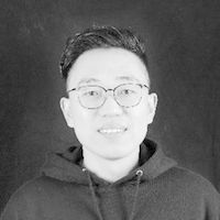 Ein Schwarz-Weiß-Porträt einer Person mit Brille und Kapuzenpullover vor einem dunklen Hintergrund.