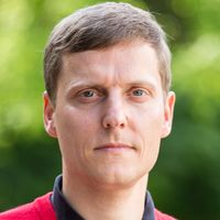 Ein Porträt eines Mannes in einem roten Pullover vor einem unscharfen grünen Hintergrund.