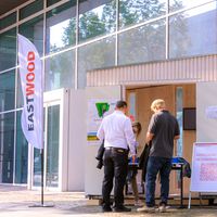 Menschen registrieren sich an einem Stand für einen Netzwerkabend vor einem modernen Gebäude.