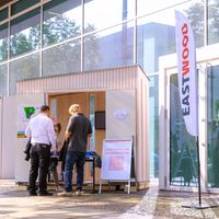 Menschen registrieren sich an einem Stand für einen Netzwerkabend vor einem modernen Gebäude.