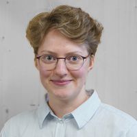 Ein Porträt einer Person mit Brille und hellem Hemd vor einem neutralen Hintergrund.