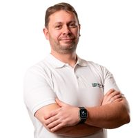 Ein Mann in einem weißen Poloshirt steht mit verschränkten Armen vor einem weißen Hintergrund.
