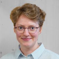 Ein Porträt einer Person mit Brille und hellem Hemd vor einem neutralen Hintergrund.