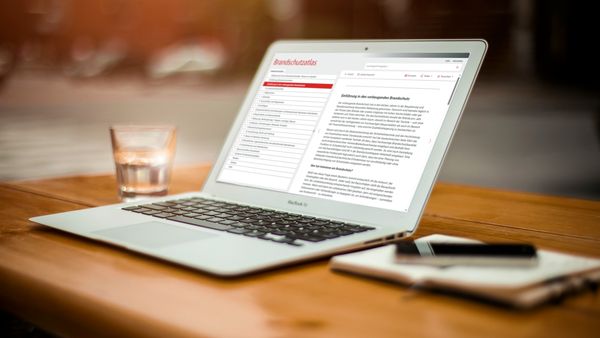 Ein Laptop auf einem Holztisch zeigt ein geöffnetes Textdokument mit Informationen zum Brandschutz.