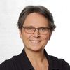 Porträt einer lächelnden Person mit Brille und kurzem Haar vor einem neutralen Hintergrund.